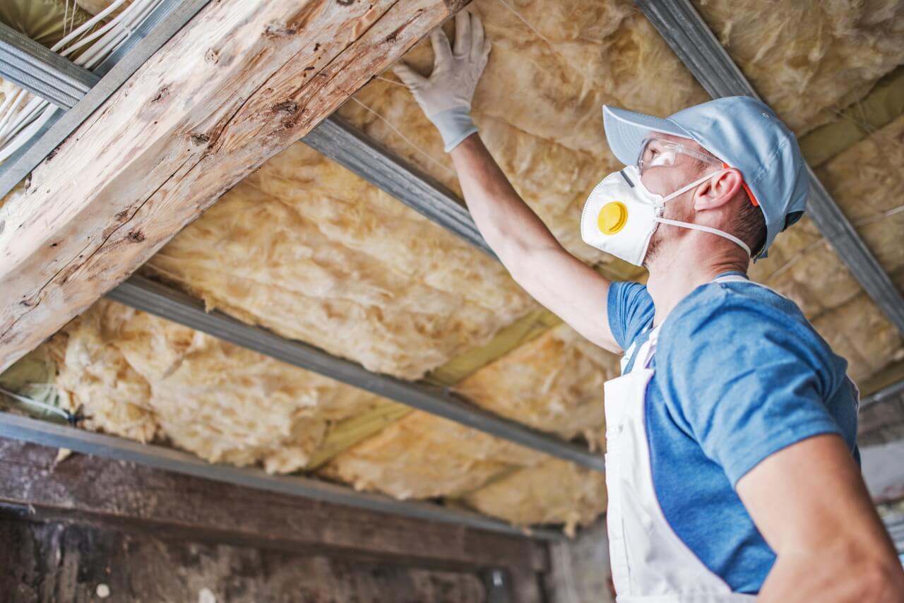 A man in a blue shirt with a mask is checking attic insulation. The right insulation will help you heat your home efficiently.
